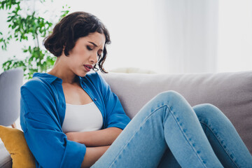 Obraz premium Young woman in casual attire relaxing indoors on a cozy couch during daylight in a modern home interior setting
