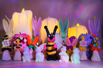 A bee figurine, gnomes and toy rabbits on the background of Easter candles.