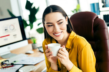 Professional woman in modern office smiling and holding coffee cup, enjoying moment of relaxation...