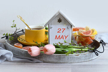 Calendar for May 27: numbers 27, name of the month May in English, tray with a cup of tea and marmalade on a light background