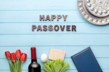 Flat lay of traditional Passover Seder symbols including tulips, red wine, matzah, egg, lettuce, and silver Seder plate on blue wooden background with &ldquo;Happy Passover&rdquo; text celebrating Jewish holiday