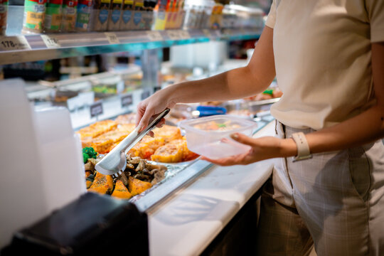 Woman serving food in supermarket using tongs and plastic container