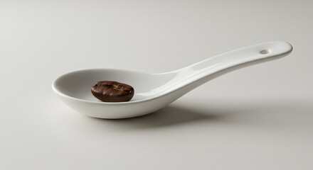 Single Roasted Coffee Bean in a White Porcelain Spoon On White Background