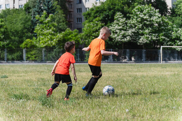 Two boys running after soccer ball on green field.