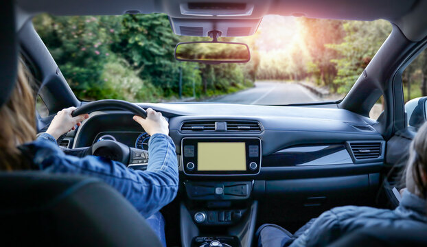 Woman driving a car and her hands on the steering wheel and dashboard. Driving a car on an asphalt road through the mountains and trees in the summer.