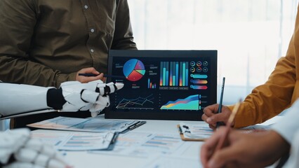 A diverse team collaborates in a modern office, discussing data analysis and insights. The robot interacts with digital displays featuring charts and graphs.Noogenesis