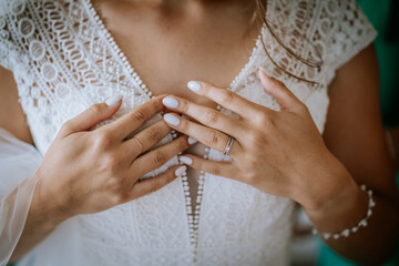 Close-up of a bride’s hands with elegant rings and manicure resting on a detailed lace wedding...