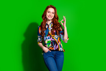 Portrait of a Red-Haired Smiling Woman Gesturing OK Sign Against Bright Green Background