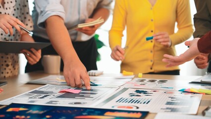 Fototapeta premium A diverse team gathers around a table in an office to discuss charts and graphs, using sticky notes for brainstorming and strategizing on a project. SACTR