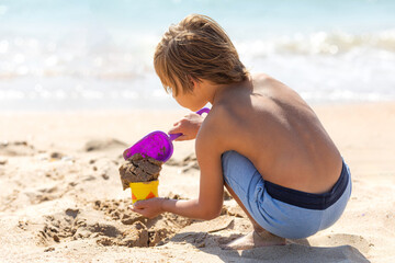 Side view child little boy playing with the sand on the beach, building sand castle, enjoying summer, playing. Advertising for tour operators, hotels, airlines. Vacation concept.