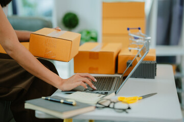 Startup SME small business entrepreneur of freelance Asian woman wearing apron using laptop and box to receive and review orders online to prepare to pack sell to customers, online sme business ideas.