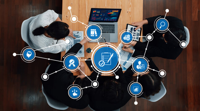 A dynamic group gathers around a wooden table, collaborating on business strategies with various technology tools, enhancing productivity through innovative ideas and data visualization. Amity