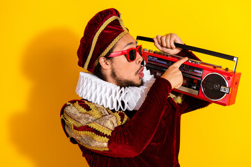 Man dressed as a nobleman in a vibrant costume holding a red boombox against a vivid yellow...