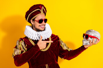Young man dressed as a duke holding a skull wearing sunglasses with a bright yellow background