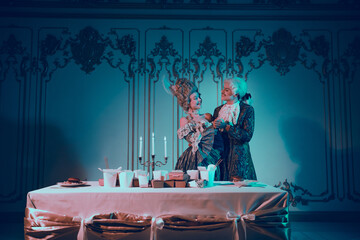 Elegant Couple in Aristocratic Costumes Beside Dinner Table Illuminated by Blue Light, Evoking...