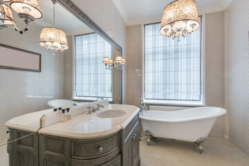 The bathroom is in neoclassical style. A mirror in a frame, elegant furniture, a bathtub with curly...