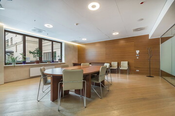 Meeting room in a modern office building. Oval wooden table and white comfortable chairs. Pots with green plants on the windowsill.