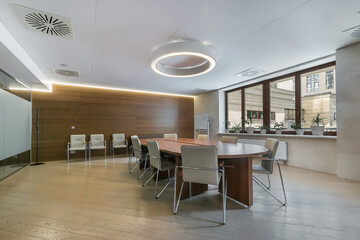 Spacious meeting room in a modern office. Comfortable chairs around an oval wooden table. Flowers on the windowsill.