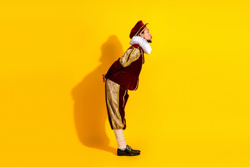 Young man in traditional nobleman costume posing against yellow background showcasing medieval...