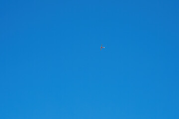 Small red airplane flying in clear blue sky
