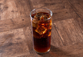 Sweet soda water with ice cubes in glass on wooden table