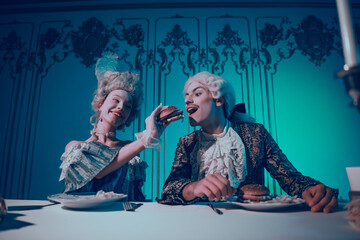 Couple in elaborate period costumes enjoying burgers in a baroque-style room with neon lighting