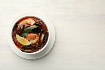 Delicious seafood soup in bowl on light wooden table, top view. Space for text