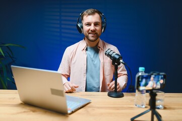 A video blogger records content in his studio. The host of the video blog is a young man who is...