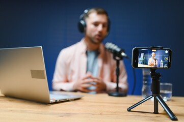A video blogger records content in his studio. The host of the video blog is a young man who is...