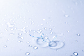 Pair of contact lenses and water drops on light mirror surface, closeup