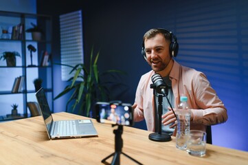 Man podcaster influencer blogger smiling while broadcasting his live audio podcast in studio using...