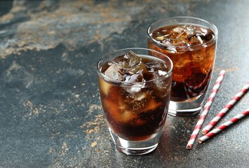 Refreshing cola with ice cubes in glasses and straws on color marble table, closeup. Space for text