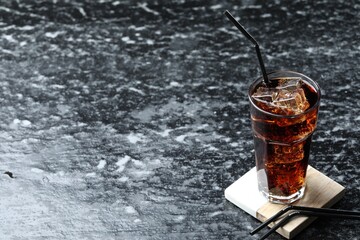 Refreshing cola with ice cubes and straw in glass on dark textured table. Space for text