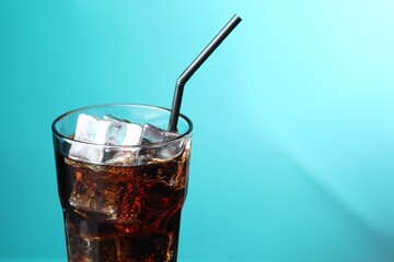 Refreshing cola with ice cubes and straw in glass on turquoise gradient background, closeup. Space for text