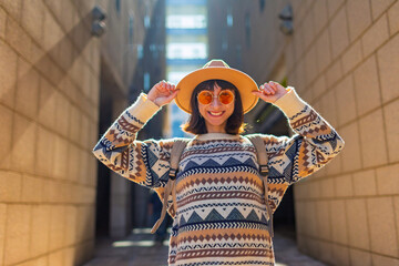 portrait of a stylish girl with a backpack in the city. happy young woman walking along the street among the buildings. female traveler with a backpack explores the city.