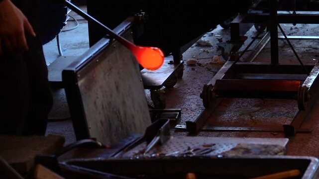 Glassblower at work with hot glass using a blowpipe and melting in an oven.