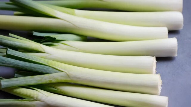 Close-up of fresh whole leeks stacked horizontally, showcasing their green leaves and cylindrical white stalks in a food photography setting
