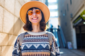 portrait of a stylish girl with a backpack in the city. happy young woman walking along the street among the buildings. female traveler with a backpack explores the city.