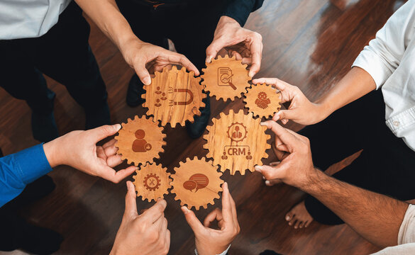 Hands assemble wooden gears symbolizing teamwork and CRM strategies in a business setting. This image emphasizes collaboration, communication, and efficient workflow. Amity