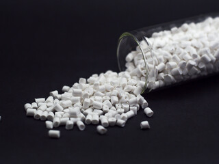 White masterbatch granules with glass tube spilled on black background. Perfect for plastic company...