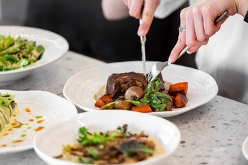 A plate with freshly cooked meat, garnished with vegetables like mushrooms and carrots, served on a dining table with other dishes in view. Captures dining and food preparation.