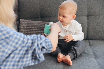 Mother giving drink to her little son sitting on sofa