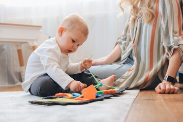 Baby boy playing with educational toy developing fine motor skills with mother watching at home