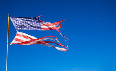 Tatterted and torn American Flag flying against a blue sky