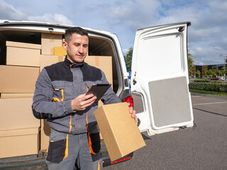Delivery worker in uniform stands at the back of a van full of packages, scanning a parcel with a...