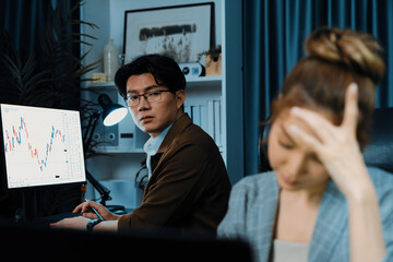 Stressful businesswoman looking at computer stock exchange via email with coworker working at back...
