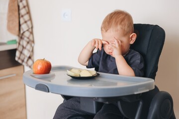 Baby rubbing eyes sitting in highchair refusing to eat apple slices