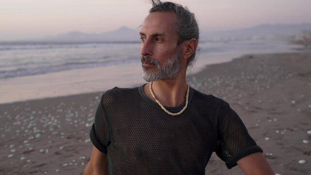 Mature yoga instructor practicing mindfulness and breathing exercises on a serene beach as the sunset