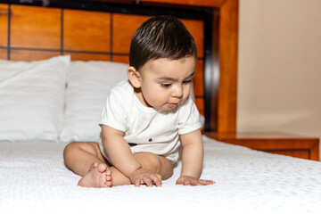 Baby sitting on a bed, crouching and supporting himself with his hands as if he were looking for something