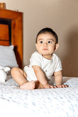 baby sitting and leaning on a bed with a serious face